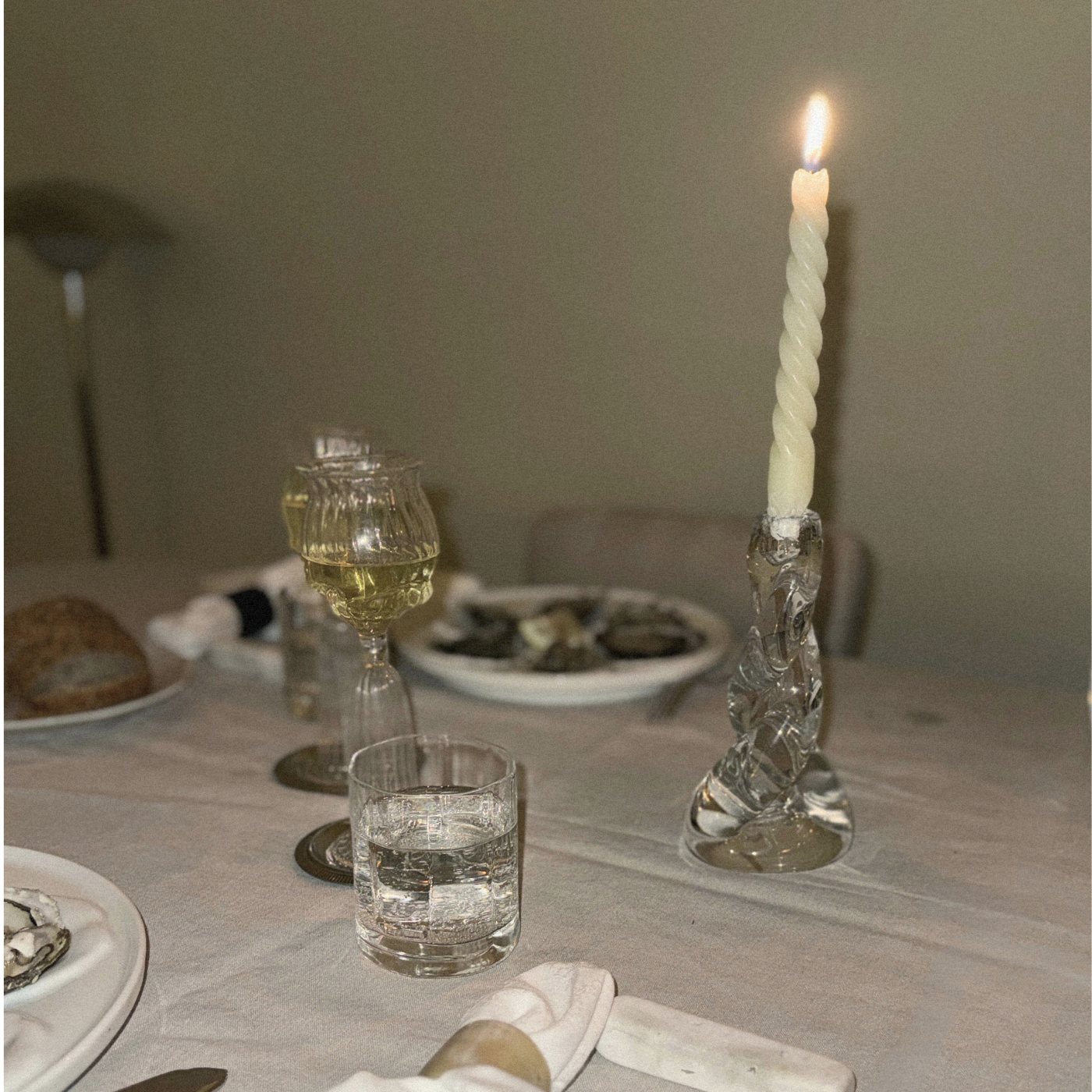 Dining table setting with glasses, a candle, and food on a neutral background thomas oyster