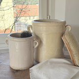 Two beige antique Italian ceramic pots on a wooden surface with a window in the background