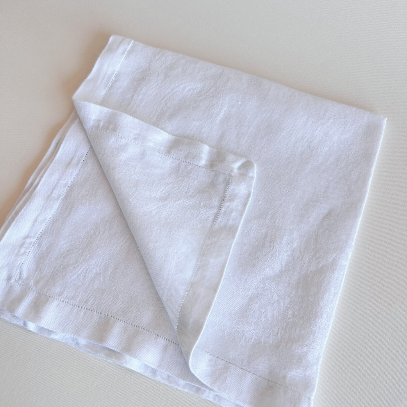 White jacquard cotton napkin folded on a beige background with napkin ring