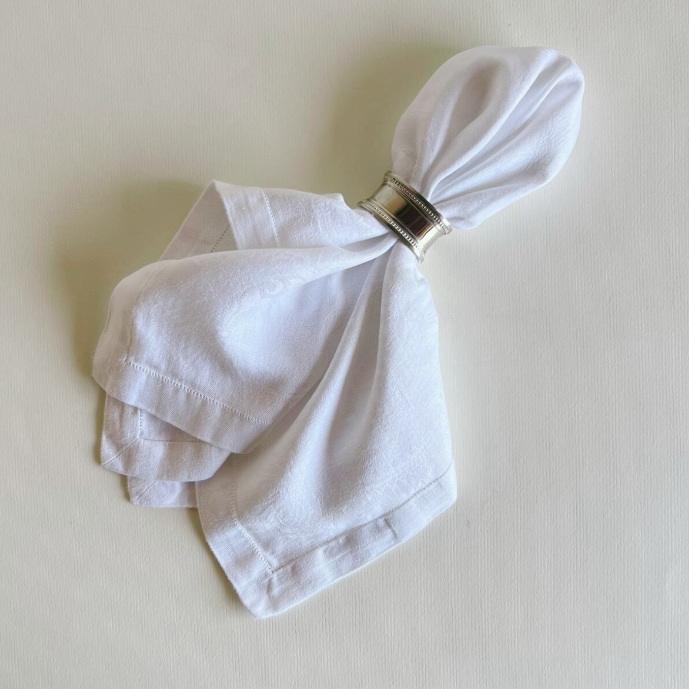 White jacquard cotton napkin folded on a beige background with napkin ring