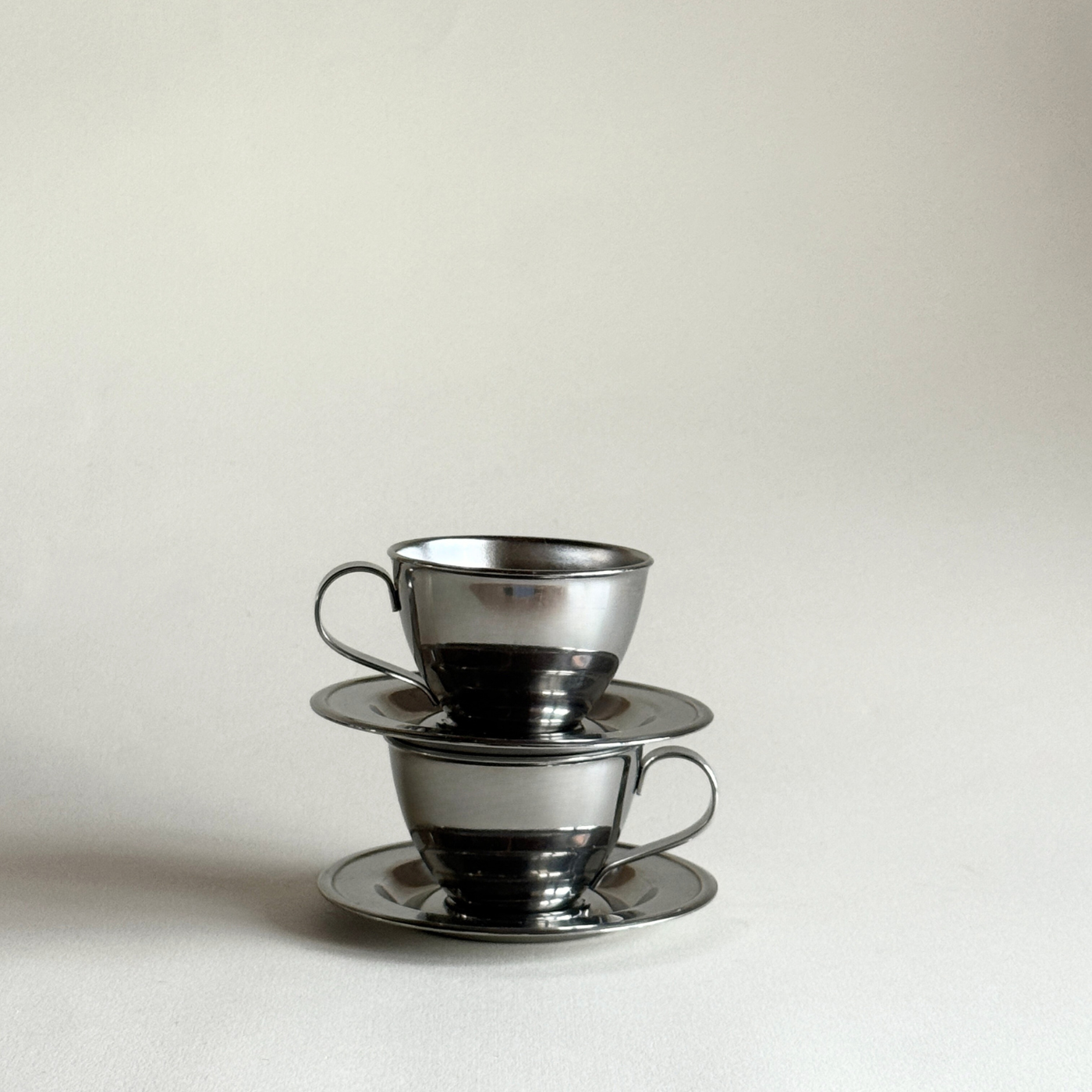 Two silver teacups with saucers on a light gray background P&B nanni