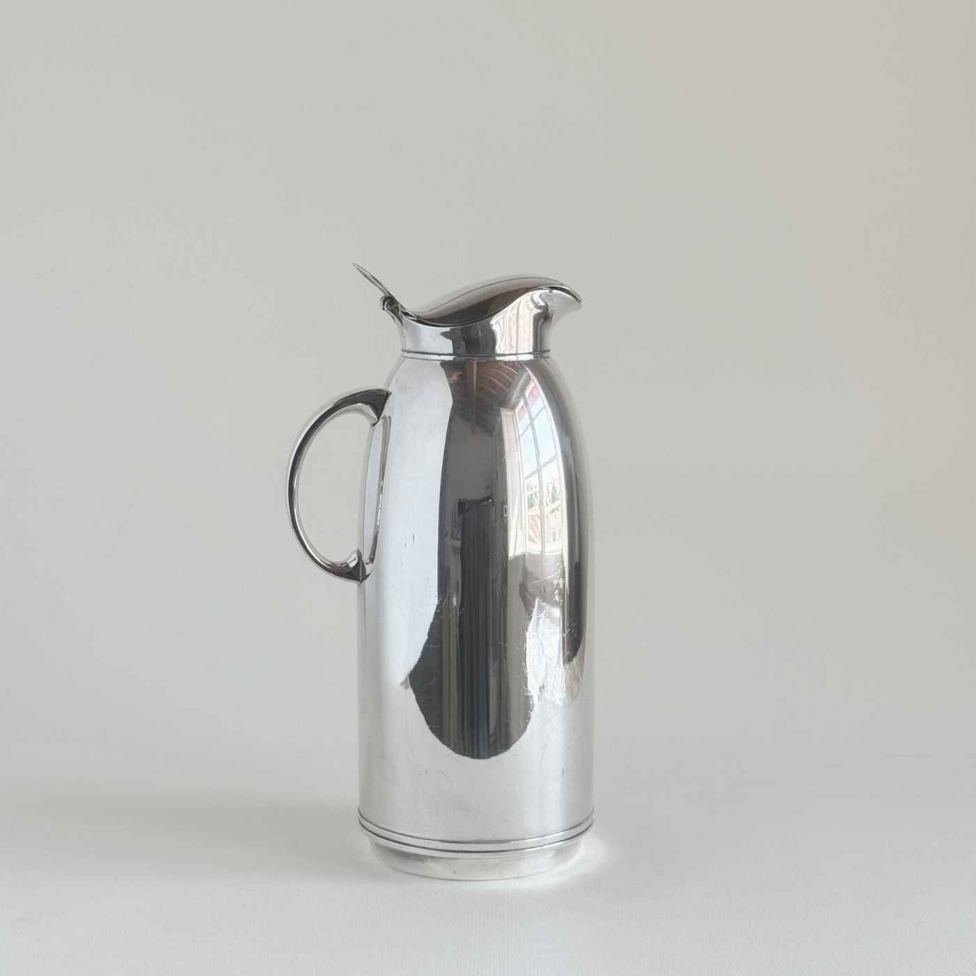 Silver plated thermos jug — front three-quarter view showing mirror-polished body, circular loop handle and hinged flip-top lid, Italian 1970s