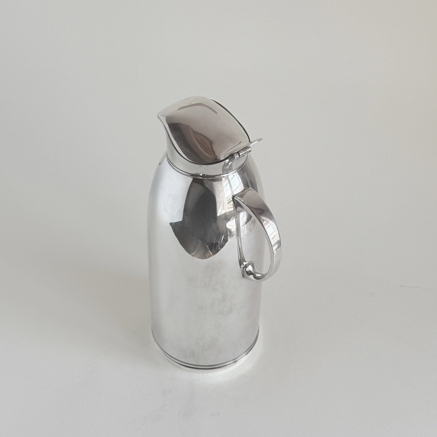 Silver plated thermos jug — close-up of mirror-polished body showing micro-scratches consistent with regular use