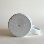 White ceramic mug with speckled texture on a beige background pentik