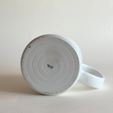 White ceramic mug with speckled texture on a beige background pentik