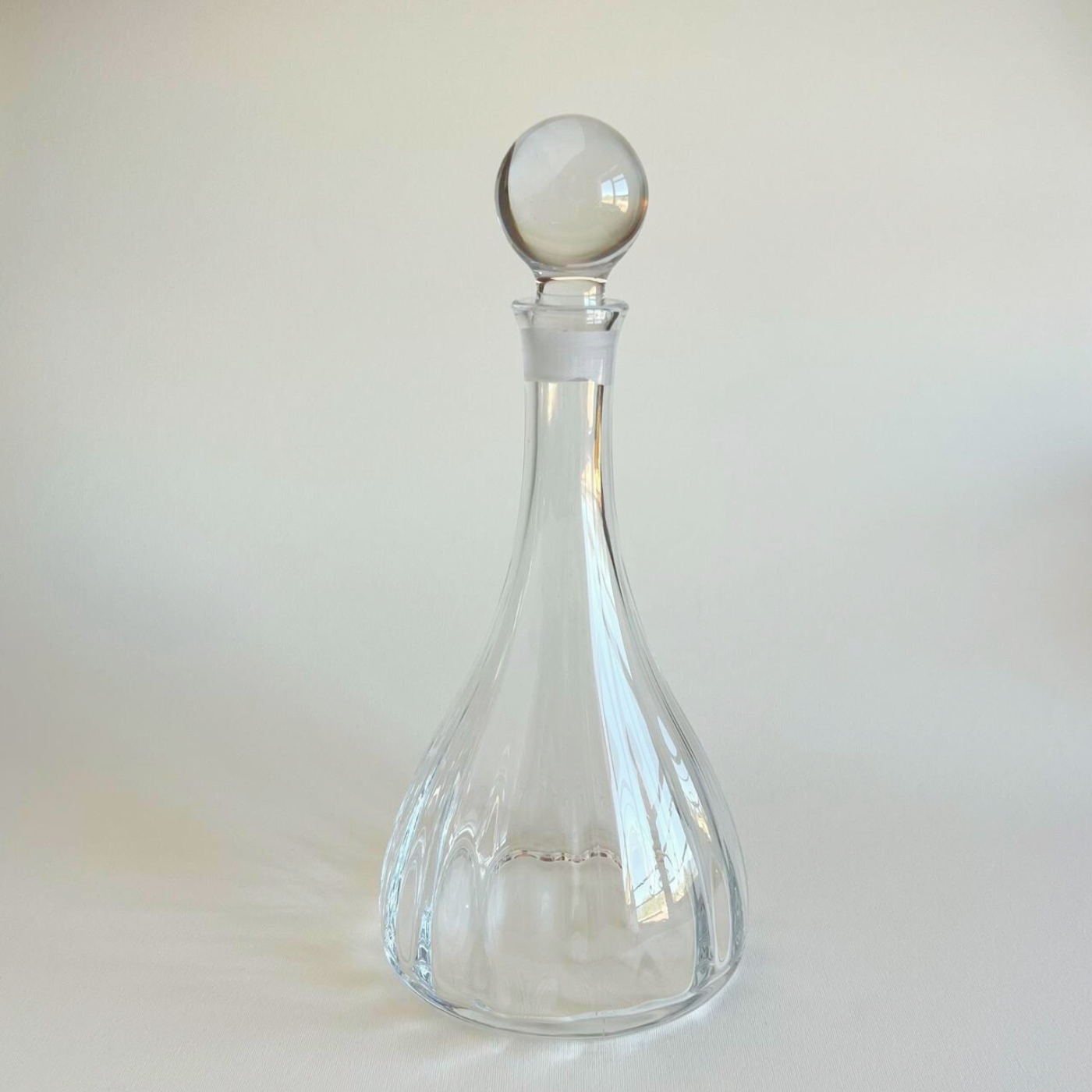 Clear glass decanter with a spherical stopper on a light beige background