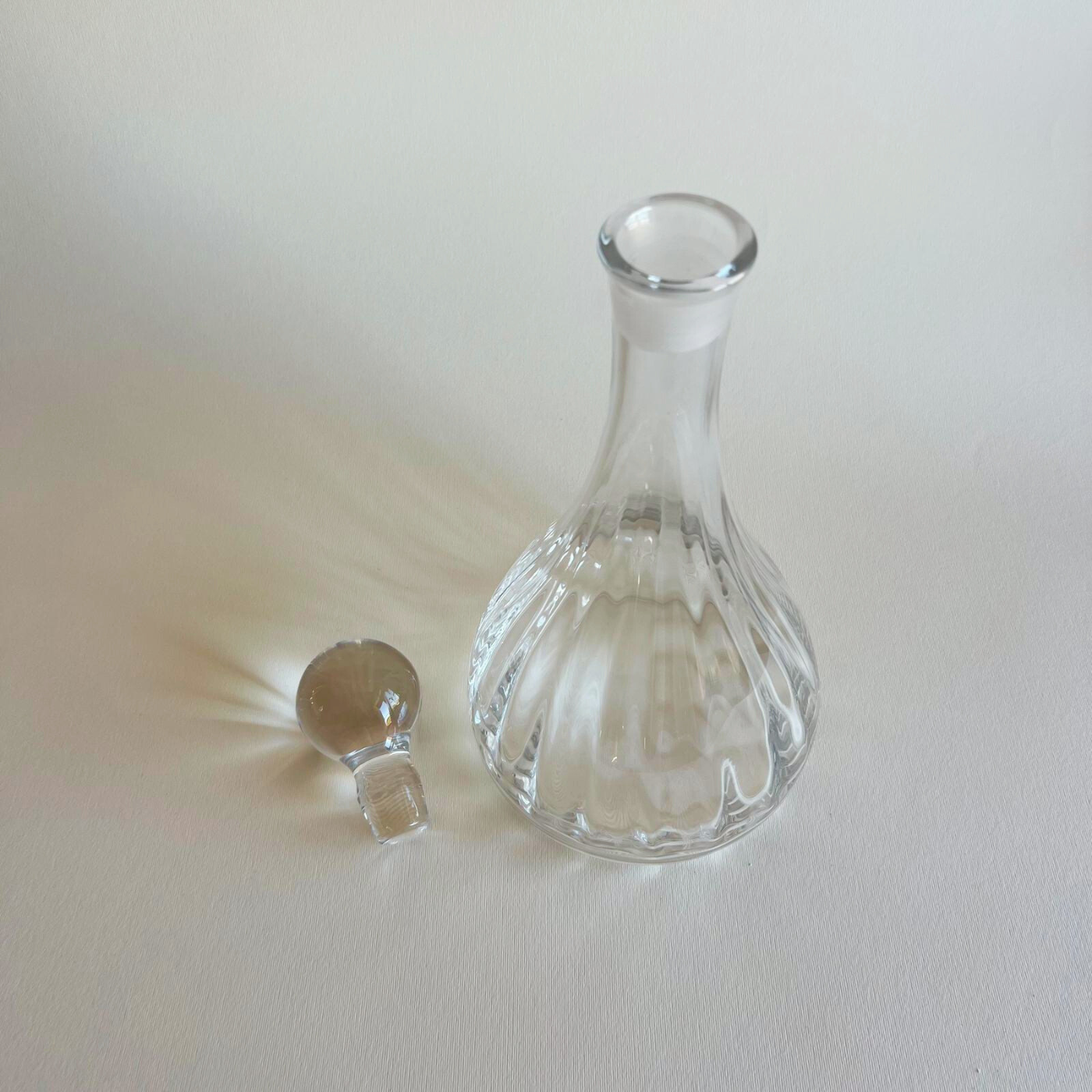 Clear glass decanter with a spherical stopper on a light beige background