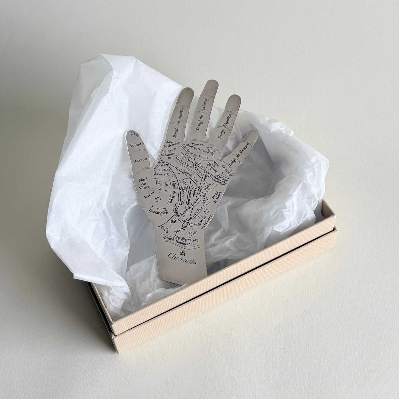 Decorative hand-shaped silver paper weight with engraved text in a box on a light background christofle hand of destiny