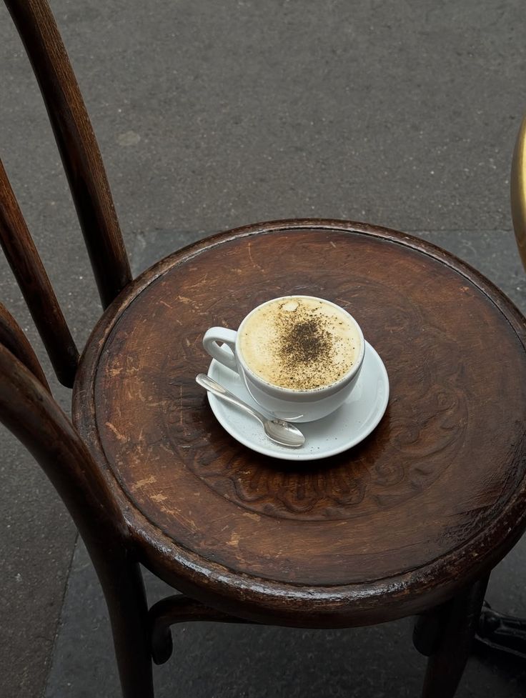 Cappuccino on a saucer with a spoon on a wooden table outdoors