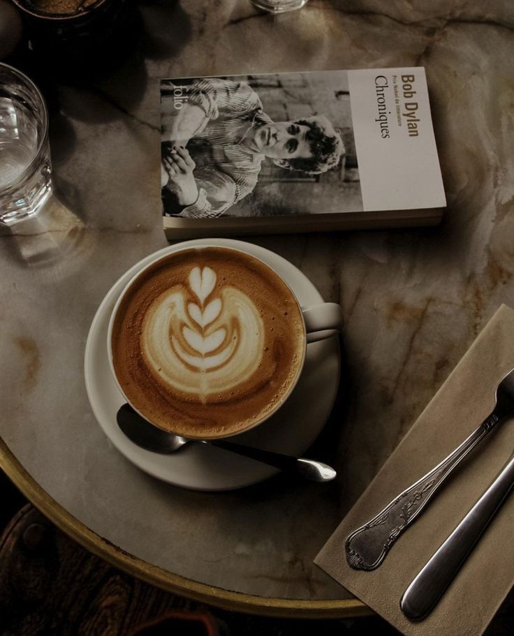 flat white coffee with latte art on a marble table with a book and glasses.