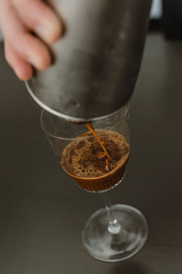 Pouring coffee from ashaker into a glass on a dark surface