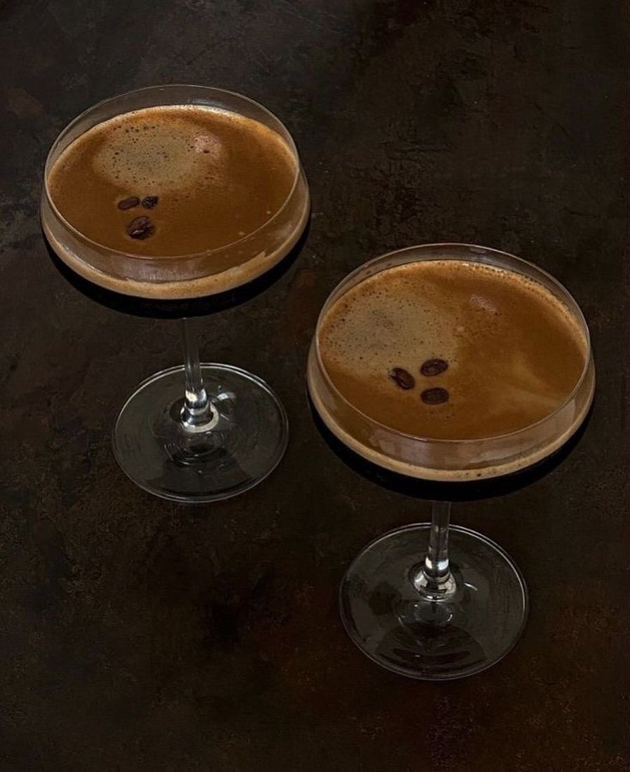 Two espresso martinis with coffee beans on a dark surface