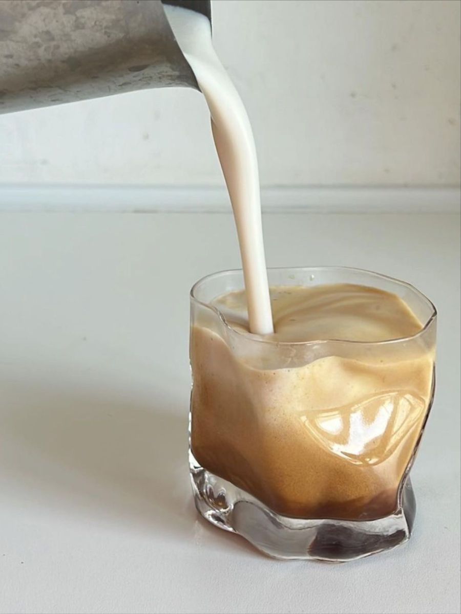 Milky liquid being poured into a glass of coffee on a white surface