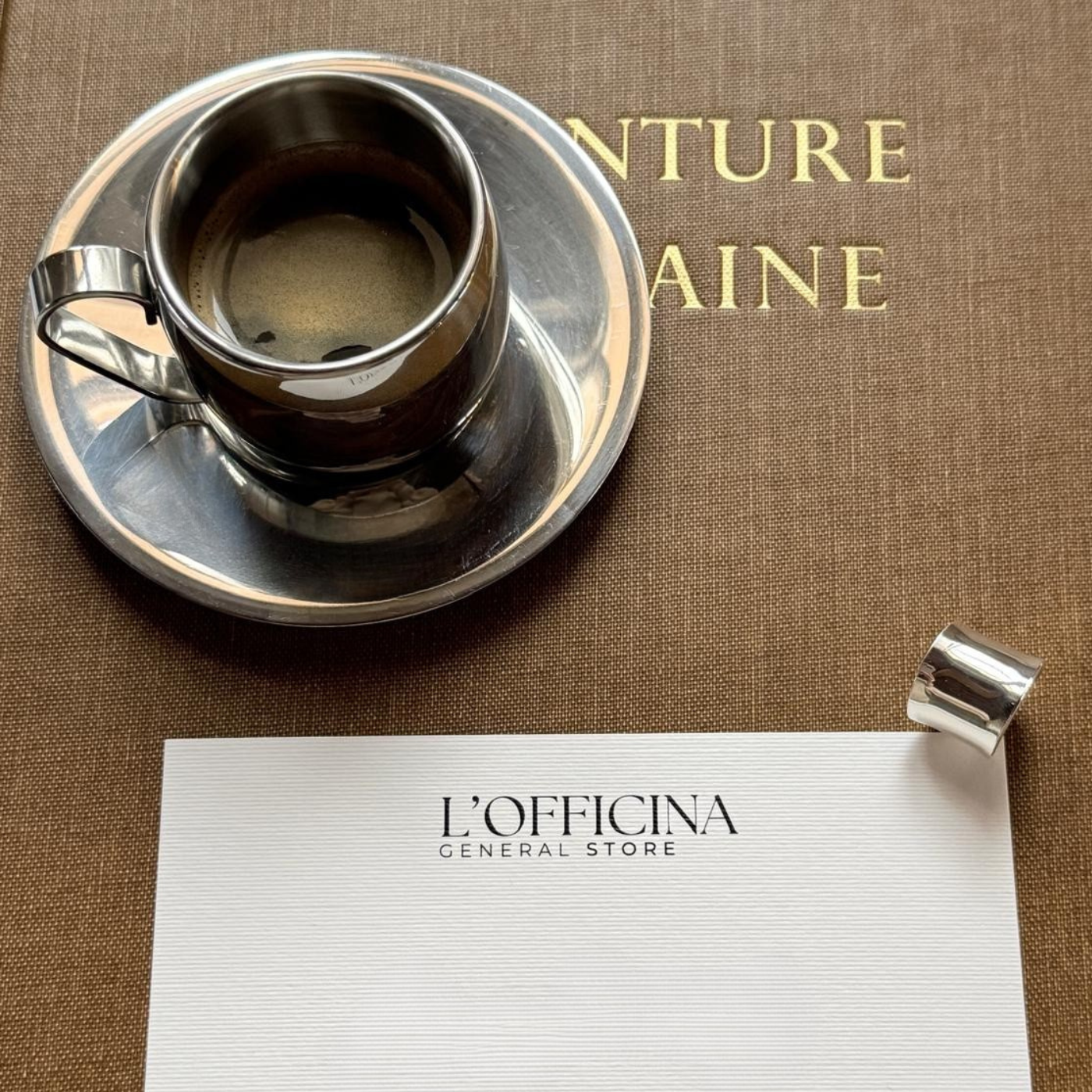 Espresso cup and saucer on a brown surface with 'L'Officina General Store' paper.
