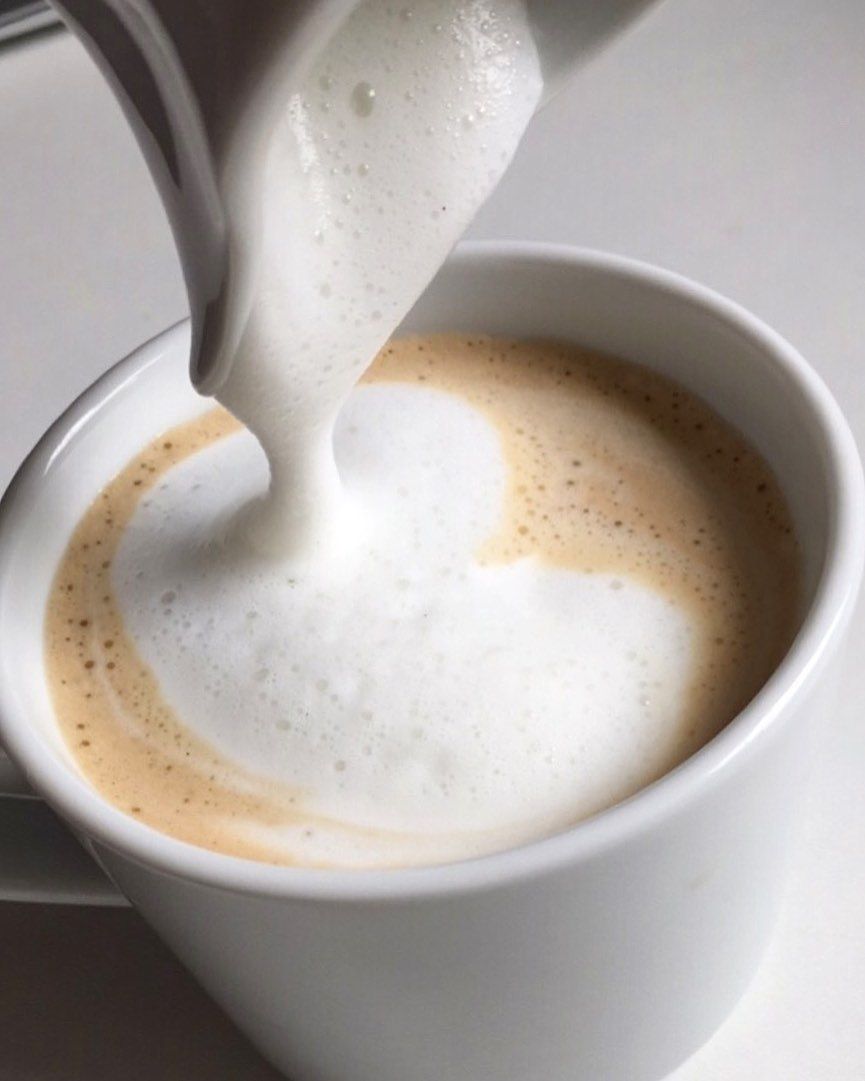 Foamy milk being poured into a cup of coffee macchiato