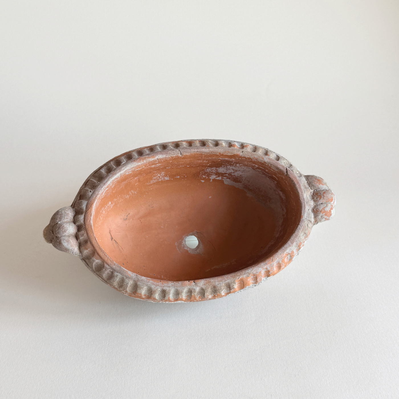 Small unglazed terracotta oval pot with drainage hole and wabi-sabi patina on a windowsill