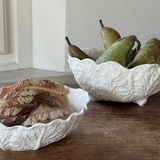 Two white ceramic bowls (wedgwood country ware and spode) with bread and pears on a wooden surface.