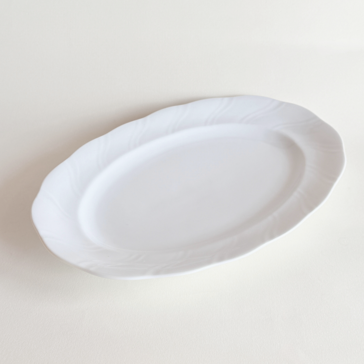 Side profile of white oval porcelain serving dish — low lip, 3 cm height, foot ring base